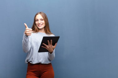 Mavi duvarda tableti olan genç ve güzel bir kadın.