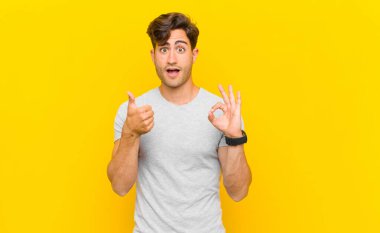  Mutlu, şaşkın, tatmin olmuş ve şaşırmış hissediyorum, tamam gösteriyor ve başparmaklarını hareket ettiriyor, gülümsüyor