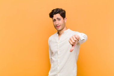 Huysuz, sinirli, sinirli, hayal kırıklığına uğramış ya da canı sıkkın genç bir adam, turuncu arka planda ciddi bir görünüm sergiliyor.