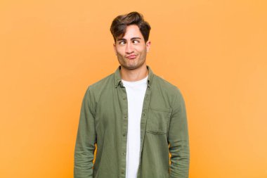 Aptal bakışlı, aptal ve komik görünen genç bir adam. Şaşı bakışlı, şaka yapan ve turuncu arka planda takılan.