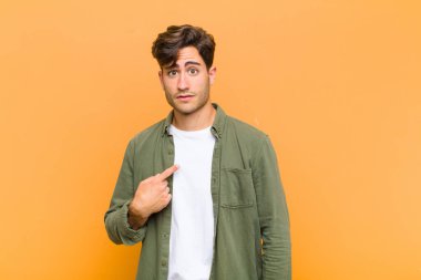 Kafası karışmış, kafası karışmış ve kendine güveni olmayan genç yakışıklı bir adam kendini gösterip kim olduğumu soruyor, ben mi? turuncu arkaplan
