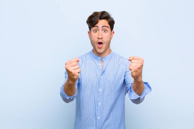 Genç ve yakışıklı bir adam inanılmaz bir başarıyı kutluyor. Kazanan gibi, heyecanlı ve mutlu görünüyor. Al bakalım! mavi arkaplan