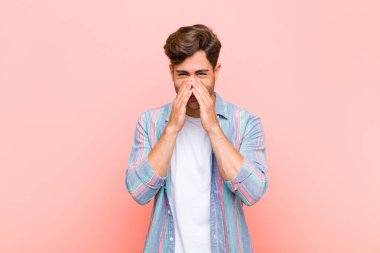 Genç yakışıklı adam mutlu, neşeli, şanslı ve şaşkın görünüyor. İki eli pembe arka planda olan ağzını kapatıyor.
