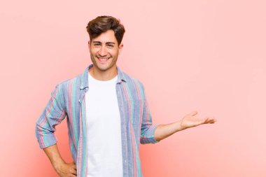 Genç yakışıklı adam gülümsüyor, kendinden emin, başarılı ve mutlu hissediyor, fotokopi alanında pembe arka plana karşı fikir veya konsept gösteriyor.