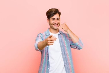 Genç yakışıklı adam neşeyle gülümsüyor ve kamerayı işaret ediyor. Daha sonra seni arayıp pembe arka planda telefonla konuşuyor.