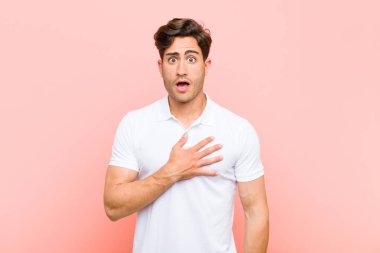 Genç yakışıklı adam şok olmuş ve şaşırmış hissediyor, gülümsüyor, el ele tutuşuyor, mutlu ya da pembe arka plana karşı minnettarlık gösteriyor.