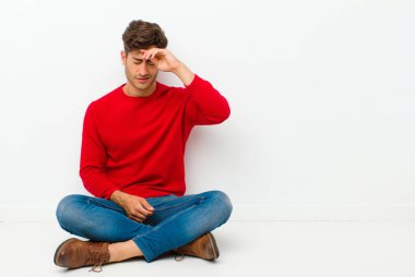Genç yakışıklı adam stresli, yorgun ve hayal kırıklığına uğramış, alnından ter damlayan, yerde otururken umutsuz ve bitkin hisseden.