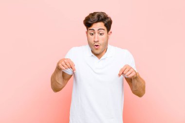 Genç yakışıklı adam şaşkın, ağzı açık ve şaşırmış, pembe arka plana karşı inançsızlık ve şaşkınlık içinde bakıyor ve işaret ediyor