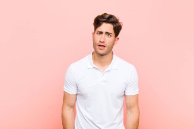Genç yakışıklı adam şaşkın ve şaşkın hissediyor, aptal, şaşkın bir ifadeyle beklenmedik bir şeye bakıyor pembe arka planda