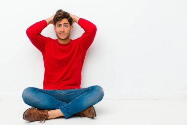 Genç yakışıklı adam kendini stresli, endişeli, endişeli ya da korkmuş hissediyor, elleri başının üstünde, yerde otururken hata yaptığı için panikliyor.