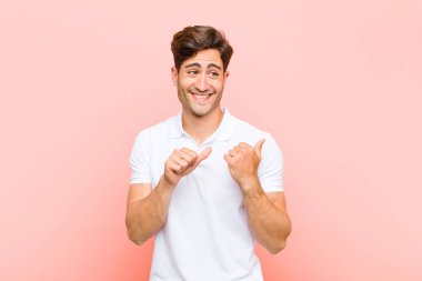 Genç yakışıklı adam neşeyle gülümsüyor ve kenardaki fotokopi alanını gösteriyor. Pembe arka planda mutlu ve tatmin olmuş hissediyor.