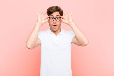 Genç yakışıklı adam şaşkın, şaşırmış ve şaşırmış hissediyor. Elinde pembe arka planda hayret dolu, inanmayan bir bakış var.