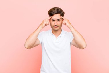 Ciddi ve konsantre görünümlü genç yakışıklı bir adam, pembe arka plana karşı beyin fırtınası yapıyor ve kafa yoruyor.