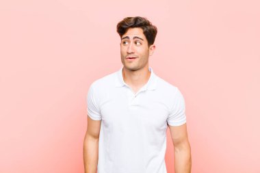 Genç yakışıklı adam şaşkın, mutlu, şaşkın ve şaşırmış hissediyor, pembe arka plana karşı ağzı açık bakıyor