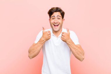 young handsome man smiling broadly looking happy, positive, confident and successful, with both thumbs up against pink background clipart