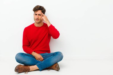 Genç yakışıklı adam kafası karışık ve şaşkın hissediyor. Deli, deli ya da aklını kaçırmış olduğunu gösteriyor. Yerde oturuyorsun.