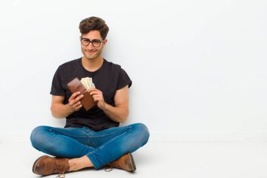 young handsome man with a wallet sitting on the floor sitting on the floor in a white room