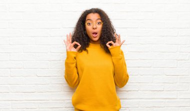 Genç siyahi kadın şok olmuş, şaşırmış ve şaşırmış hissediyor. Onaylıyor. İki eliyle tuğla duvara işaret veriyor.