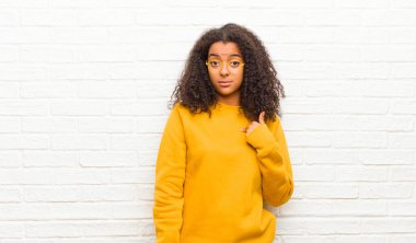 Genç siyahi kadın şaşkın, şaşkın ve güvensiz hissediyor. Kendini gösterip kim olduğumu soruyor. Ben mi? tuğla duvara karşı