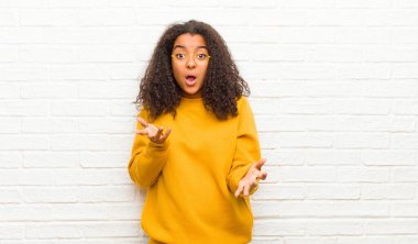 Genç siyahi kadın aşırı derecede şok olmuş, şaşırmış, endişeli ve paniklemiş hissediyor. Tuğla duvara karşı stresli ve dehşetli bir bakışla bakıyor.