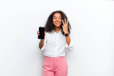 Beyaz duvarda akıllı bir telefonu olan genç, güzel siyah bir kadın.