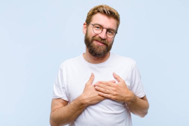 Genç, sarışın, yetişkin bir adam romantik, mutlu ve aşık, neşeyle gülümseyen ve kalbe yakın el ele tutuşan