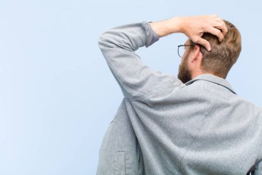 Genç, sarışın yetişkin bir adam bilgisiz ve kafası karışık hissediyor, bir çözüm düşünüyor, eli kalçasında, diğeri kafasında, dikiz aynasından.