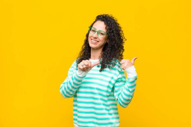 Genç, güzel bir kadın neşeli ve tesadüfen fotokopi alanını işaret ederek turuncu duvara karşı mutlu ve tatmin olmuş hissediyor.