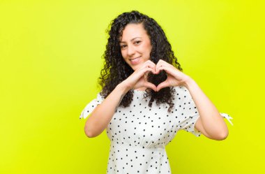 Genç ve güzel bir kadın gülümsüyor ve mutlu, sevimli, romantik ve aşık, iki eliyle krom anahtar duvarına kalp şekli veriyor.