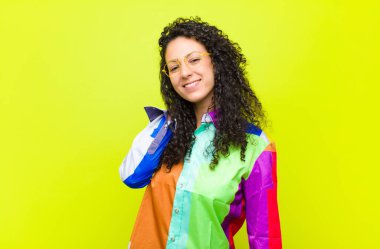 Genç, güzel bir kadın neşeli ve kendinden emin bir şekilde gülüyor. Renkli bir duvarın karşısında mutlu, dostane bir gülümsemeyle.