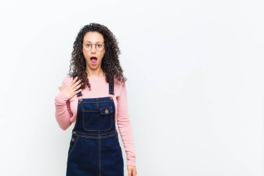 Genç, güzel bir kadın şok olmuş, şaşırmış ve şaşırmış hissediyor, elleri göğsünde ve ağzı açık, kim diyor, ben mi? Beyaz duvara yaslan