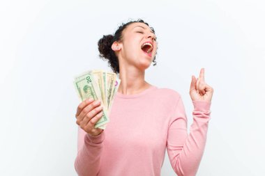 Beyaz duvarda banknotları olan genç ve güzel bir kadın.