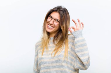 Genç ve güzel bir kadın kendini başarılı ve tatmin olmuş hissediyor, ağzı açık gülümsüyor, beyaz arka planda elle işaret veriyor.