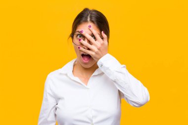 Genç iş kadını şok olmuş, korkmuş ya da korkmuş görünüyordu. Yüzü elle kaplıydı ve parmaklarının arasından turuncu duvara bakıyordu.