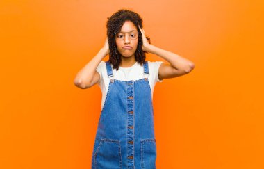 Genç, güzel, siyah bir kadın aptal ve komik görünüyor. Aptal şaşı bir ifadeyle, şakalaşıyor ve turuncu duvarın etrafında takılıyor.