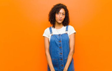 Genç, güzel siyah kadın dudaklarını birbirine bastırıyor. Tatlı, eğlenceli, mutlu, sevimli bir yüz ifadesiyle. Turuncu duvara bir öpücük yolluyor.