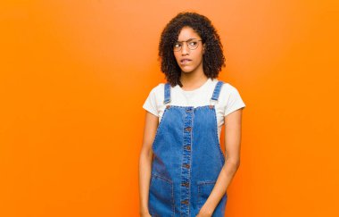 Genç, güzel, siyah bir kadın kendini cahil, kafası karışık ve hangisini seçeceği belli olmayan turuncu duvara karşı sorunu çözmeye çalışıyor.