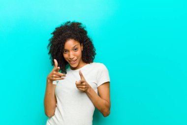 Genç siyah kadın kendini mutlu, sakin, tatmin olmuş, rahat ve başarılı hissediyor, kameraya bakıyor, mavi duvara karşı seni seçiyor.