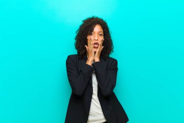 Genç siyahi kadın şok olmuş ve korkmuş hissediyor. Ağzı açık ve elleri mavi duvarda.