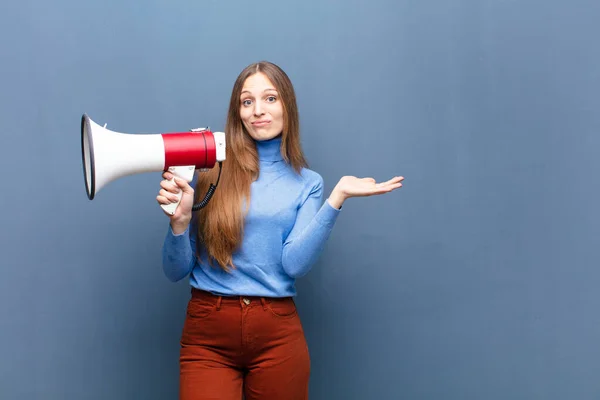 young pretty woman with a megaphone against blue wall with a copy space