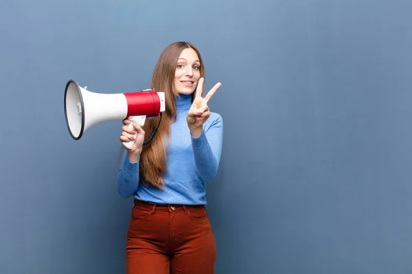 young pretty woman with a megaphone against blue wall with a copy space