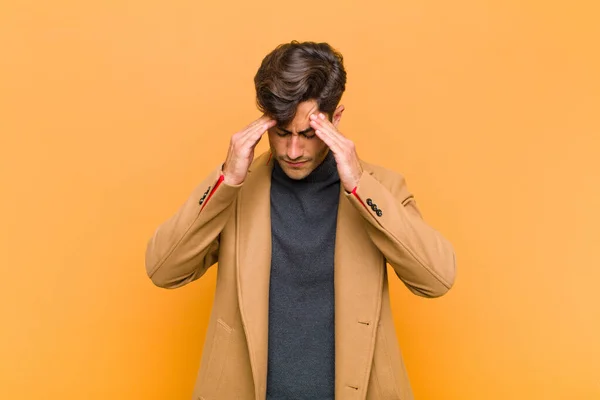 young handsome man looking stressed and frustrated, working under pressure with a headache and troubled with problems against orange background