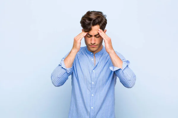ストレスを感じてフラストレーションを感じている若いハンサムな男は頭痛の種でプレッシャーの中で働いていて青い背景の問題に悩まされています — ストック写真