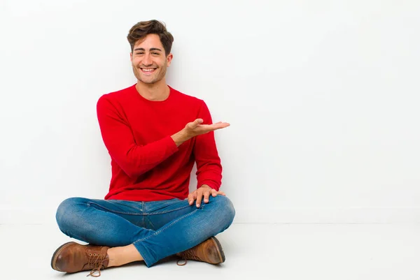若いハンサムな男は陽気に笑って幸せを感じ 床に座っ手の手のひらでコピースペースで概念を示す — ストック写真