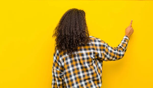 若いアフリカ系アメリカ人の女性がコピースペースを指差して黄色の壁に背を向けて — ストック写真