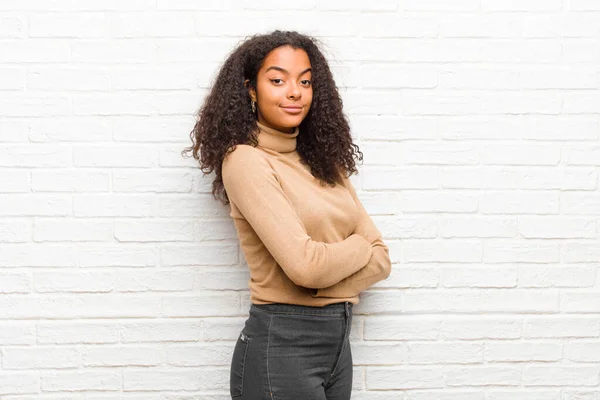 young black woman smiling to camera with crossed arms and a happy, confident, satisfied expression, lateral view against brick wall