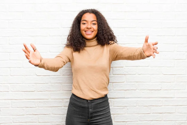 young black woman smiling cheerfully giving a warm, friendly, loving welcome hug, feeling happy and adorable against brick wall