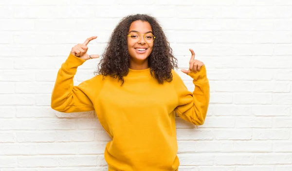 young black woman framing or outlining own smile with both hands, looking positive and happy, wellness concept against brick wall