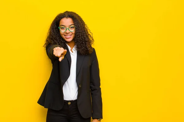 black business woman pointing at camera with a satisfied, confident, friendly smile, choosing you against orange wall