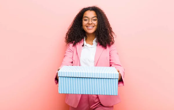 young black pretty woman with a gift box against pink wall background